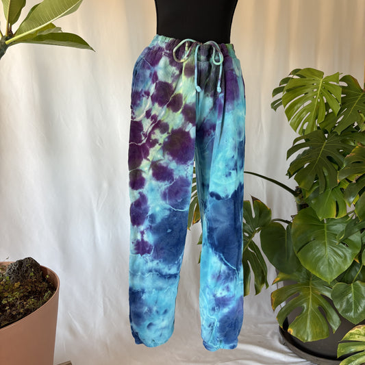 Tie-dye pants with purple and blue pattern on a white background with plants.