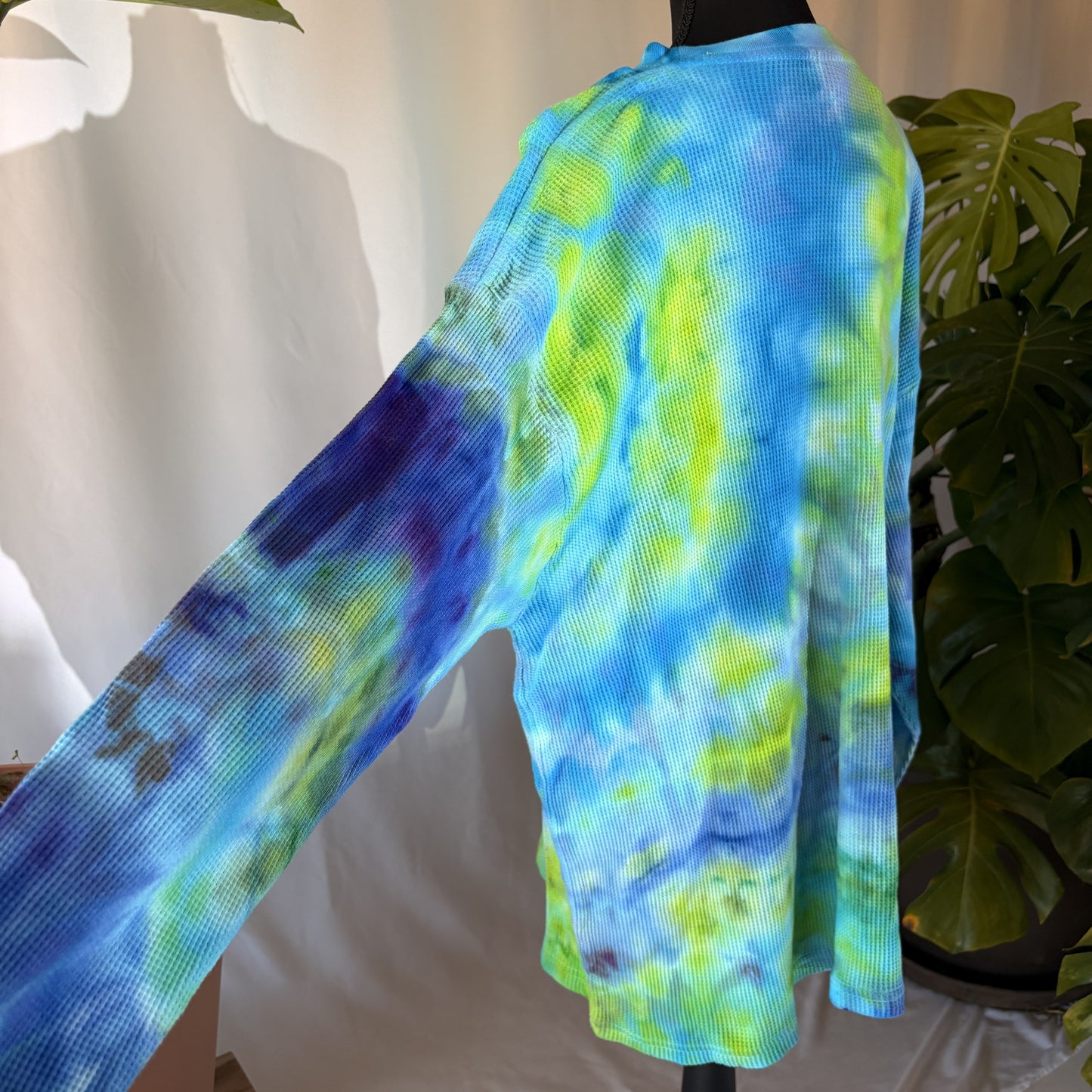 Mannequin wearing a blue and green tie-dye long sleeve with a plant in the background