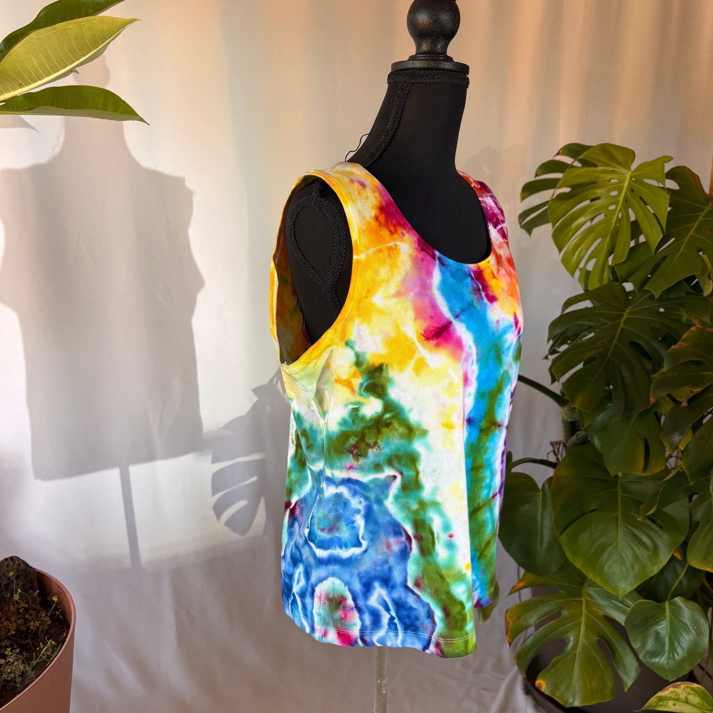 Colorful rainbow tie-dye tank top on a mannequin with plants in the background