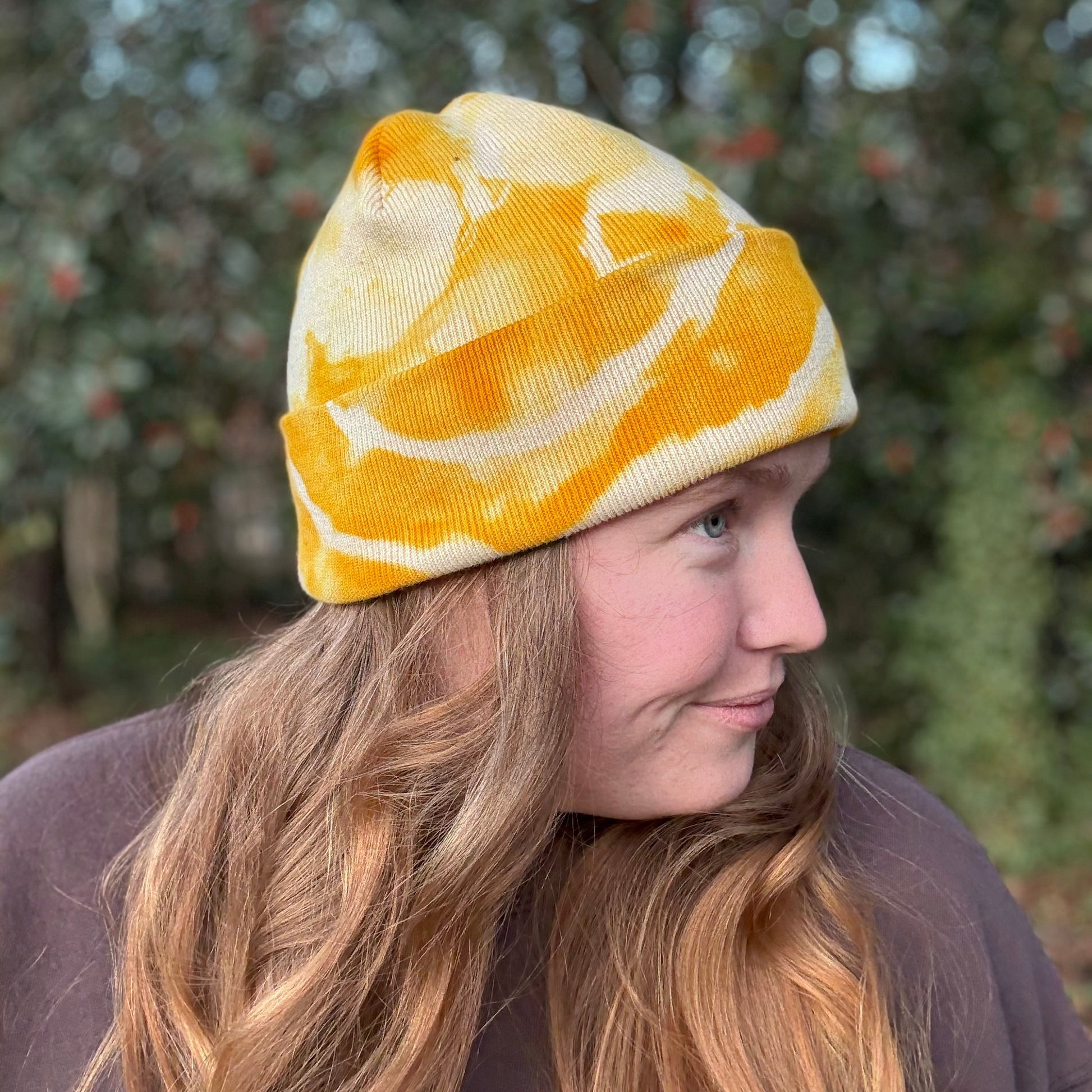 Person wearing a yellow and white patterned beanie outdoors with trees in the background