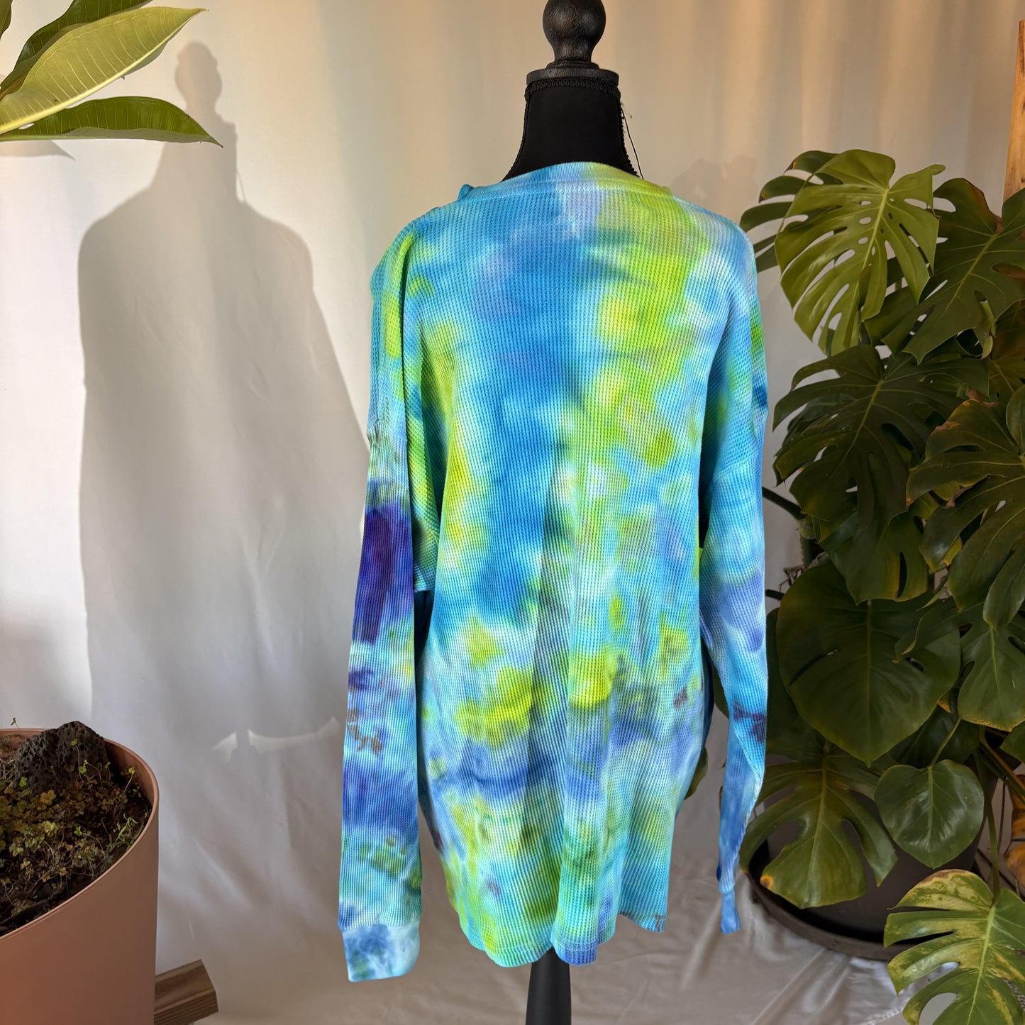 Tie-dye long-sleeve shirt on a mannequin with plants in the background
