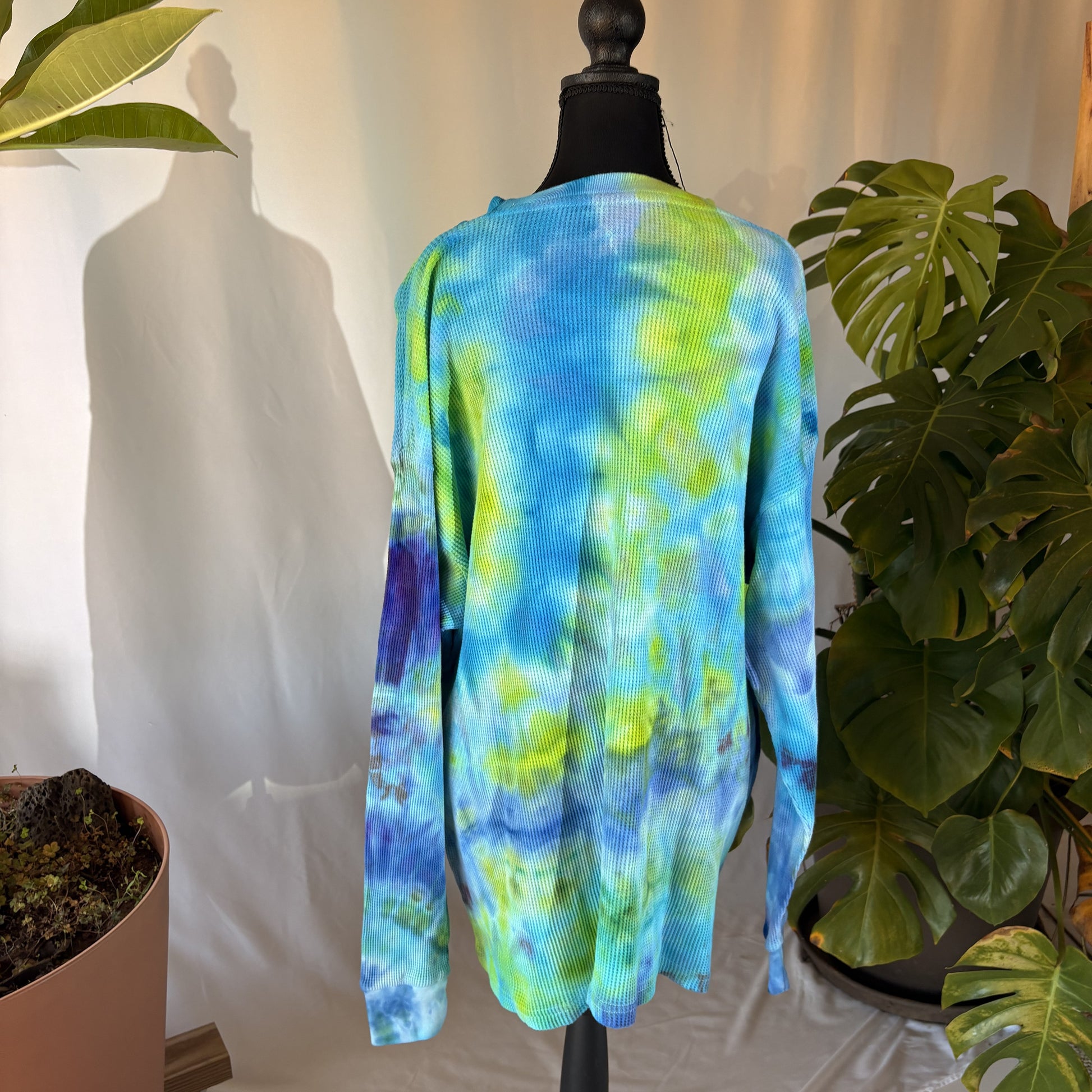 Tie-dye long-sleeve shirt on a mannequin with plants in the background